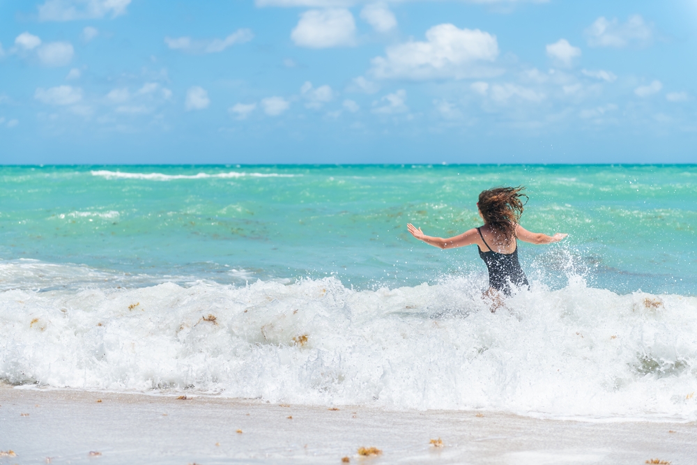 A women runs into the crash of the waves at a beach, enjoying the spray of the foam and the green-blue water in front of her. 