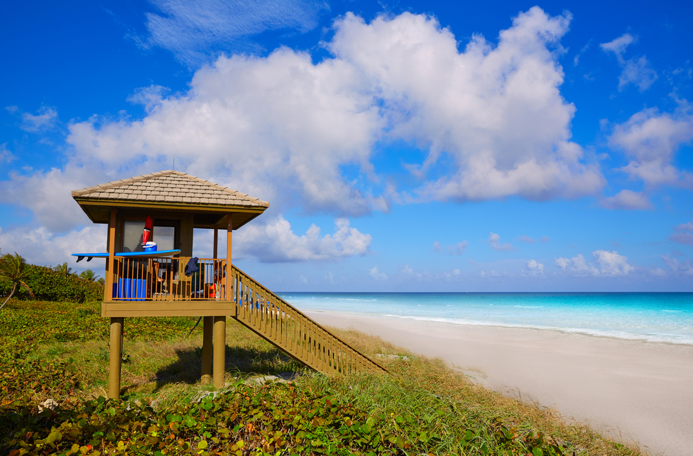 Delray Beach is one of the warmest beaches in Florida and is noted by the bright blue waters, smooth sand, and little lifeguard shacks as seen in this photo: the latter leads to a hut with a surfboard resting on the edge. 