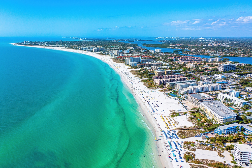 An arial shot of Siesta key shows the green-blue water as it pushes toward the white sand, and the tons of beach rentals crowded on the sand beyond hotels. This is one of the warmest beaches in Florida. 