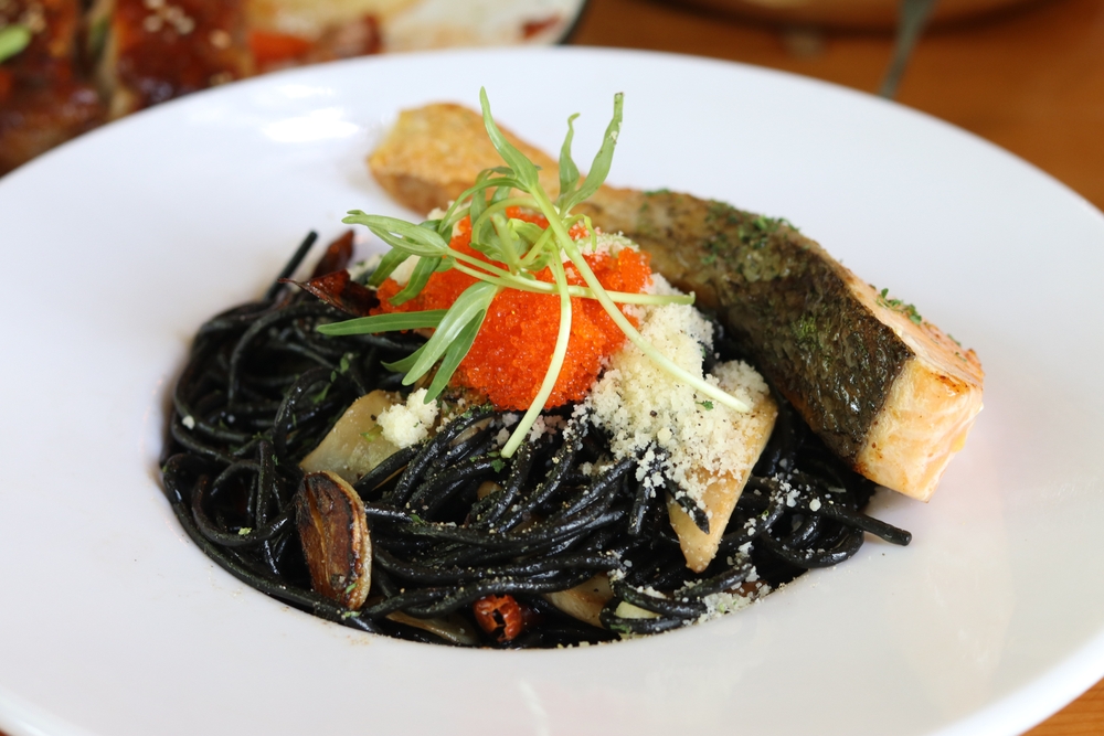 a plate of squid ink pasta with a. side of salmon and cheese