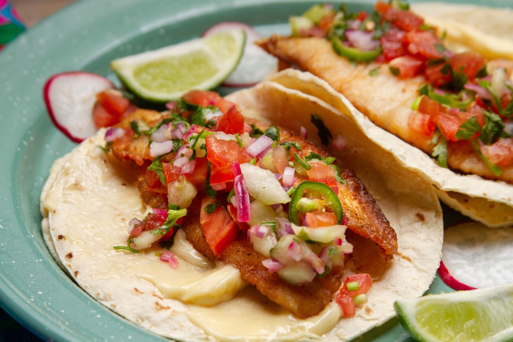 A plate with 2 tacos with fried fish with a salsa on top