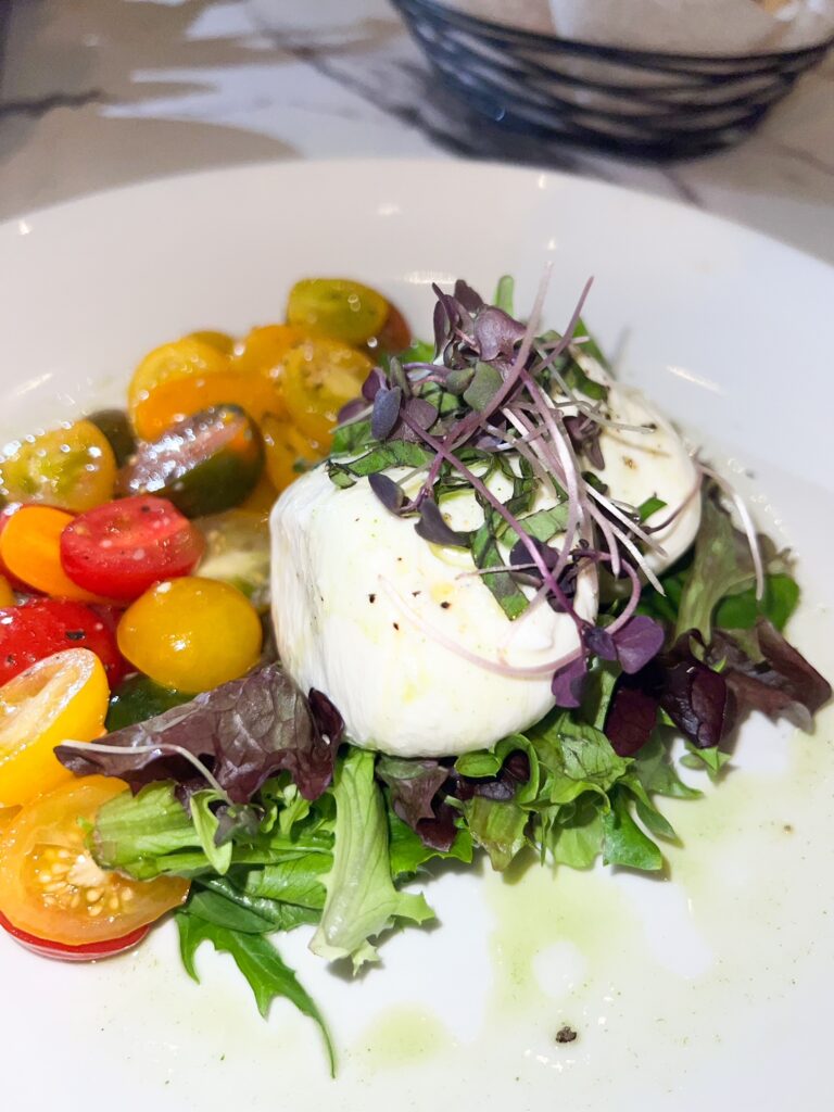 a plate of burrata with tomatoes and greens