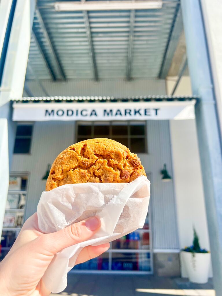 a girl with her hand holding a cookie in front of Modica Market once of the must eat at places in 30A