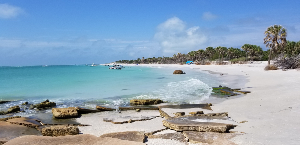 the white sand beach of Edgemont Key one of the best beaches near Tampa with broken stones and palm trees with boats in the water