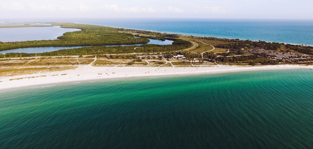 an Ariel view down on Fort De Soto beach with beautiful turquoise water, white sand, and nature preserve with river and bay In the background