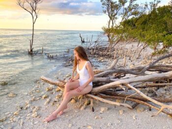 a girl in white swim suit sitting on driftwood at one the beaches near Tampa