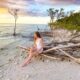 a girl in white swim suit sitting on driftwood at one the beaches near Tampa