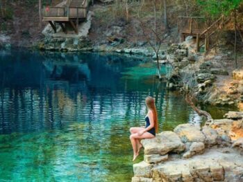 a girl in a bleu swimsuit sitting on the rock edge near one of th many Florida Springs