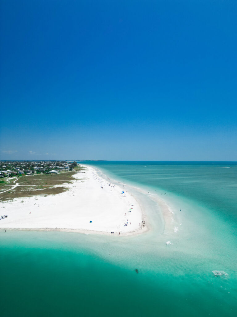 aerial photo of a white sandy beach with green space behind it and houses behind that 