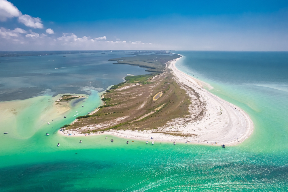 aerial photo of a white sandy beach ,the water is varying shades of green and blue, the sky is mostly clear 