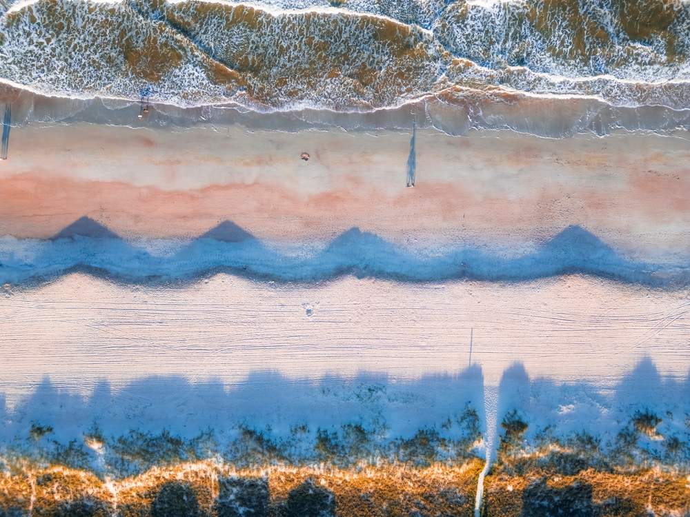 aerial photo of a white sandy beach and the sand that is wet from the waves appears to be pink 