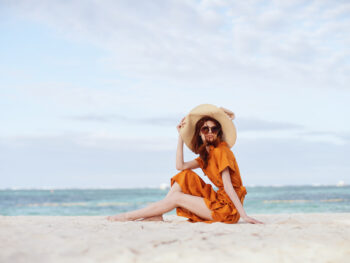 woman sitting on the beach wearing an orange dress and beige sunhat