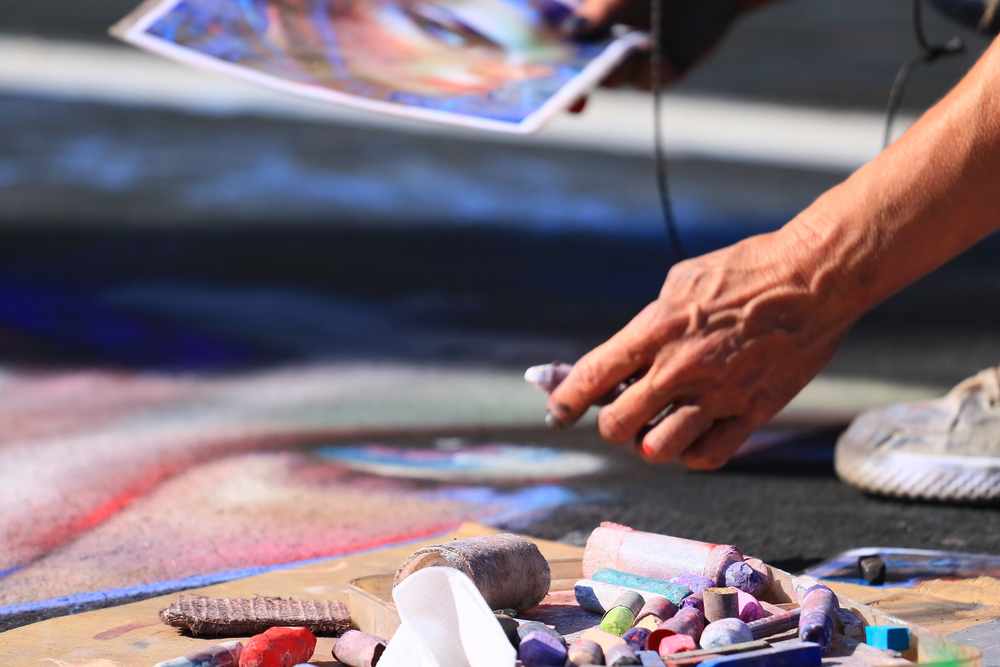 a hand is holding chalk over a large chalk drawing on the blacktop 