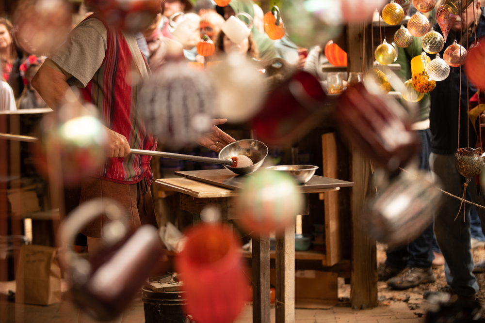 a man is standing behind hanging glass artwork doing a glass blowing demonstration 