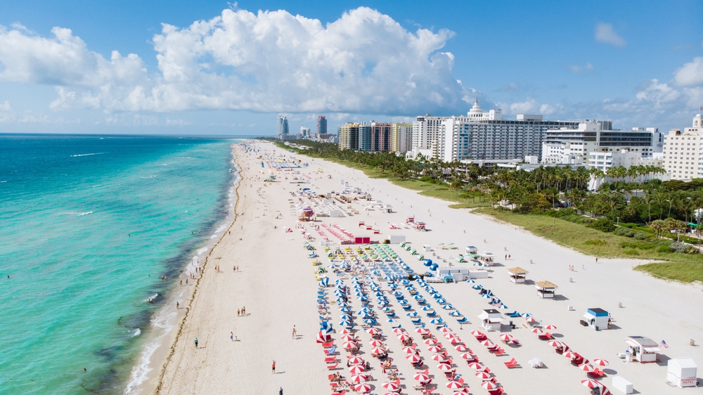 aerial photo of beach in south florida, there are beach chairs on the sand and buildings behind the beach 