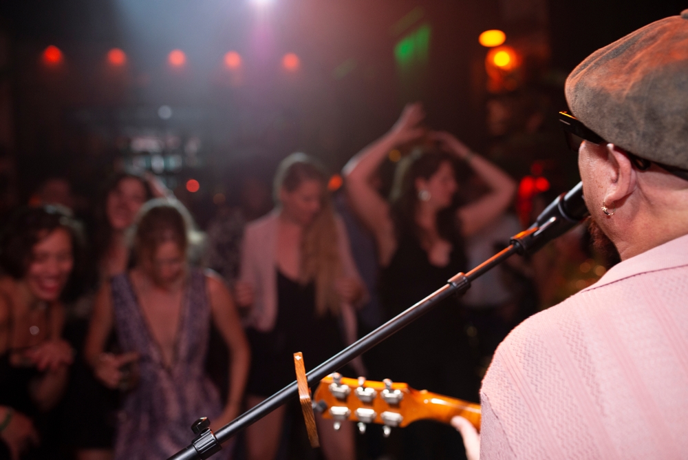 a man is standing on stage in a hat playing jazz music while women stand in front of the stage listening and dancing 