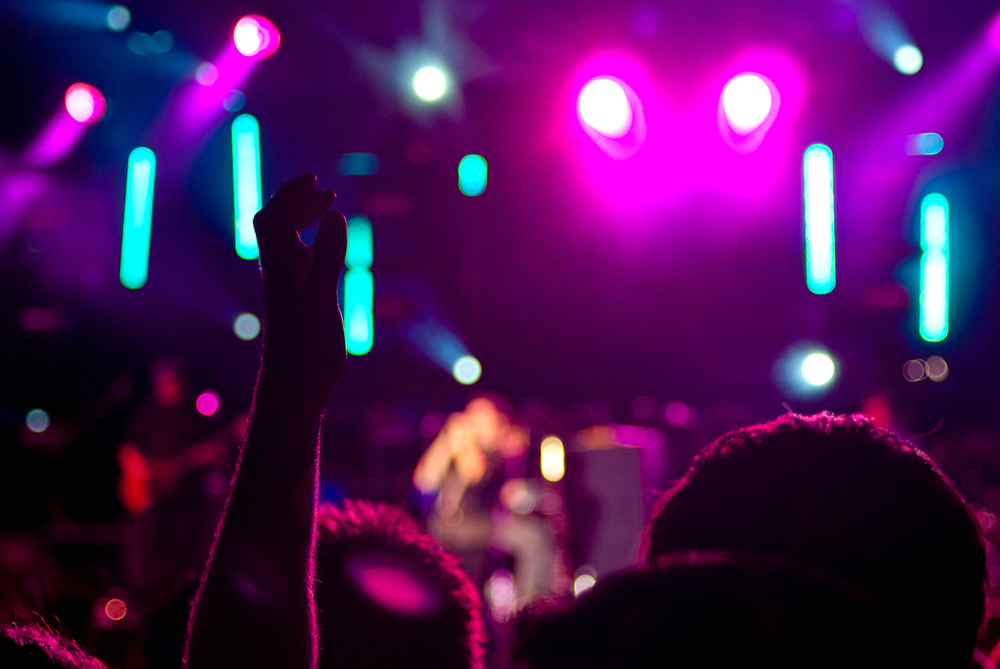 back lit music festival attendees in florida, hands are raised in the air