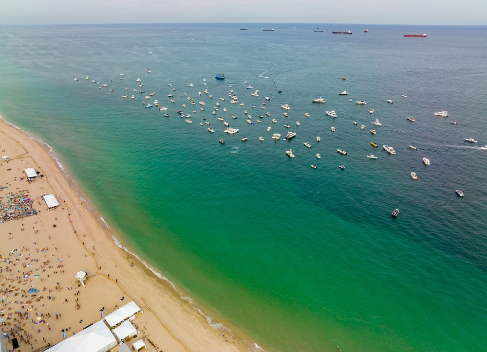 aerial photo of beach music festival and boats anchored in the water off the coast 