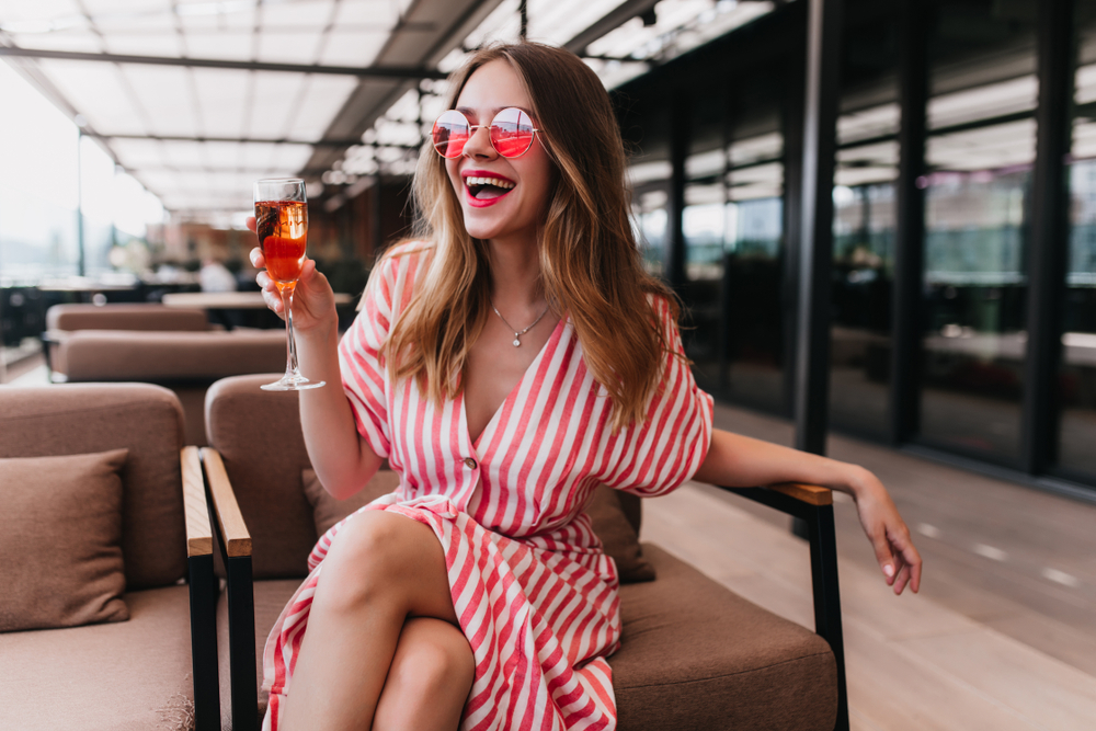 a girl in a red stripped sundress holding a glass of champagne sitting at a rooftop bar