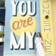 a girl in white dress standing infront of a you are my sunshine mural