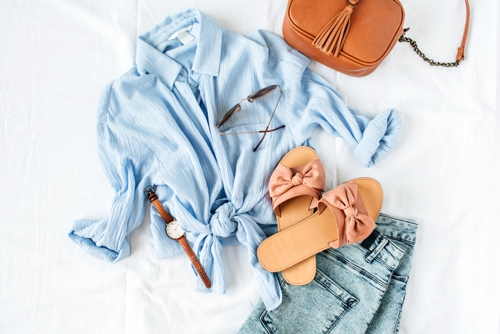 a blue button down blouse and jeans are paired with brown sandals, sunglasses and a crossbody bag. 