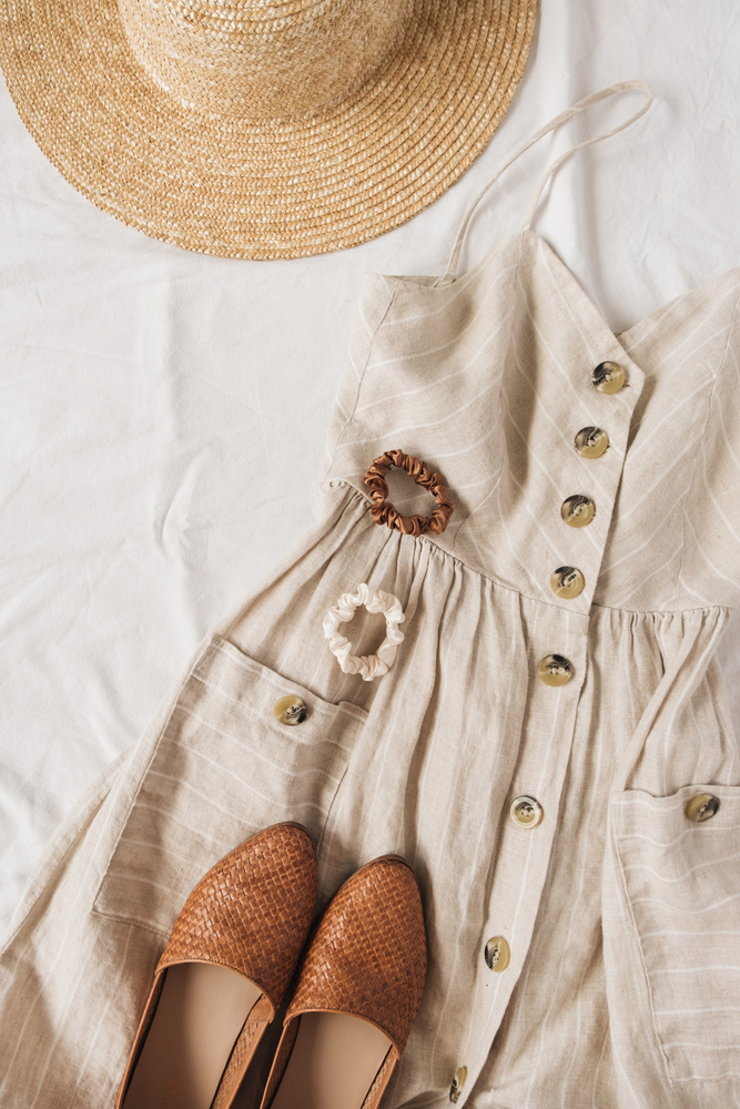 A flowy, beige dress with matching floats and hair ties and a straw hat is laid across a bed, ready to be worn in Florida spring. 