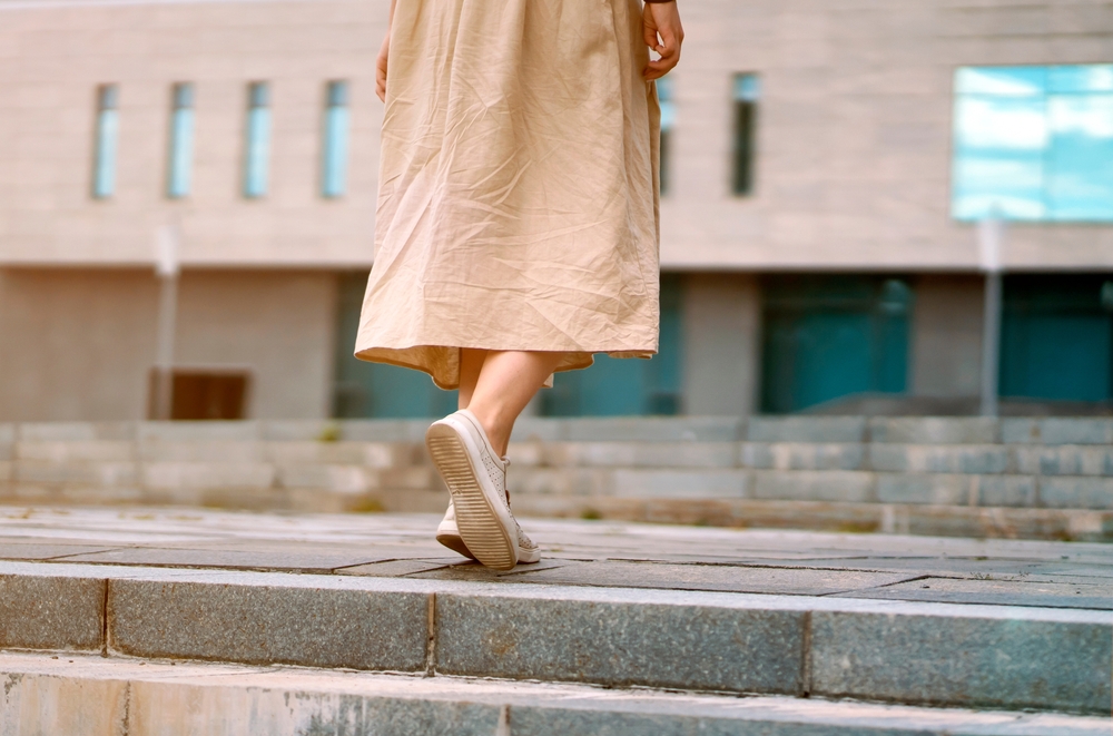 A women walks up a set of stairs, exploring downtown, in a linen skirt and comfortable walking shoes.