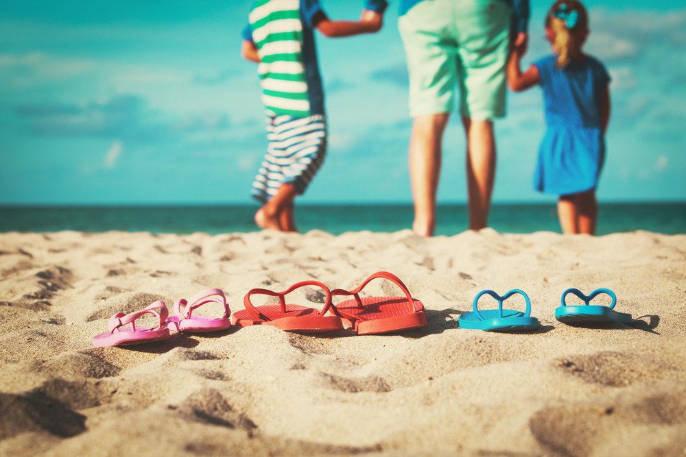 A family leaves their flip flops in the sand as they walk toward the blue water of the beach. 