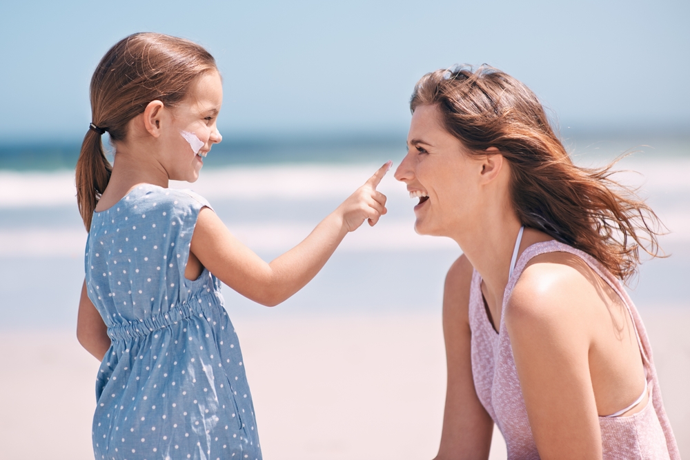 A daughter "boops" her mother on the nose with sunscreen while on the beach, because it is important to not only pack clothes when considering what to wear in Florida in spring: sunscreen is your best friend! 