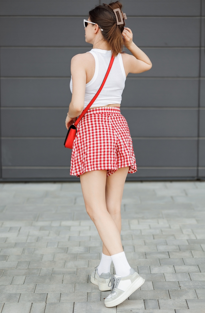 A woman faces away from the camera with her hair in a clip, her red and white checked shorts on, and a matching red crossbag on her arm, styling and knowing what to wear in Key West. 