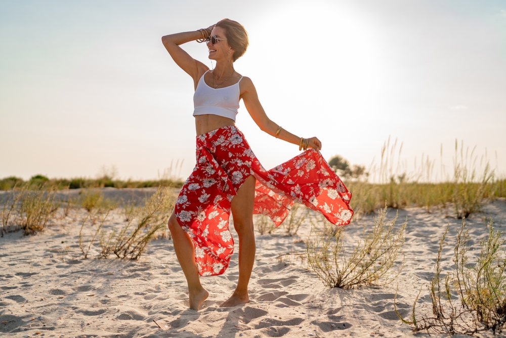 A young woman stands on a beach in a white tank top and red floral skirt, which is perfect for beach days when trying to figure out what to wear in Miami. 