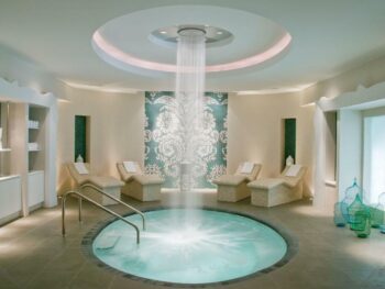 beautiful indoor hot tub with waterfall from the ceiling. the room is round with relaxing spa chairs around it.