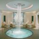 beautiful indoor hot tub with waterfall from the ceiling. the room is round with relaxing spa chairs around it.