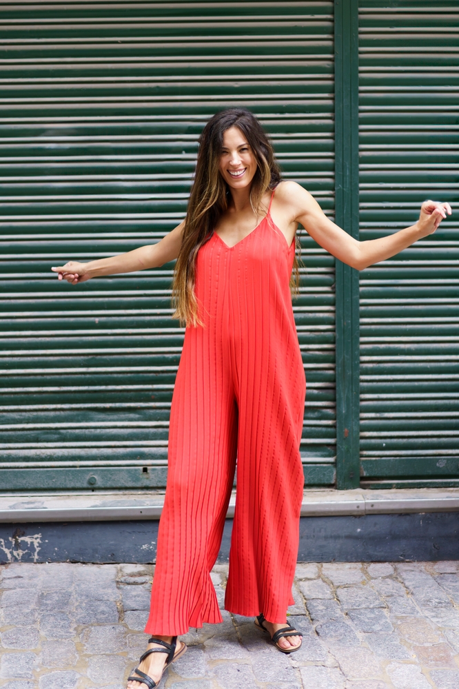 A woman smiles as she dances on the streets of Orlando: her spaghetti strap orange jumpsuit has her cool and comfortable, perfect for what to wear in Orlando. 