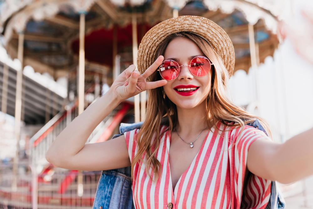 woman standing in front of a carnival ride wearing heart shaped sunglasses