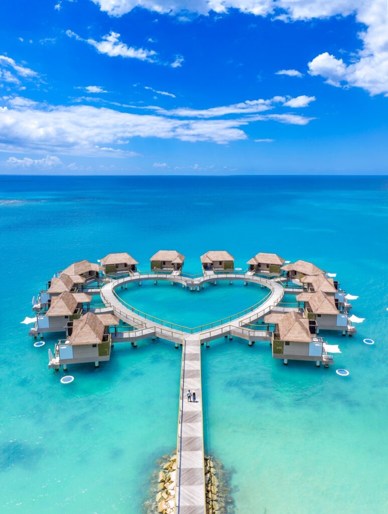 Two people walking on a boardwalk towards some overwater bungalows near Florida, They are shaped in a love heart 