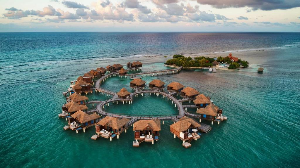 overwater bungalows with thatched roofs in a heart shape. it is sunset out so the sky is cloudy but the colors are pretty, reminiscent of the Caribbean