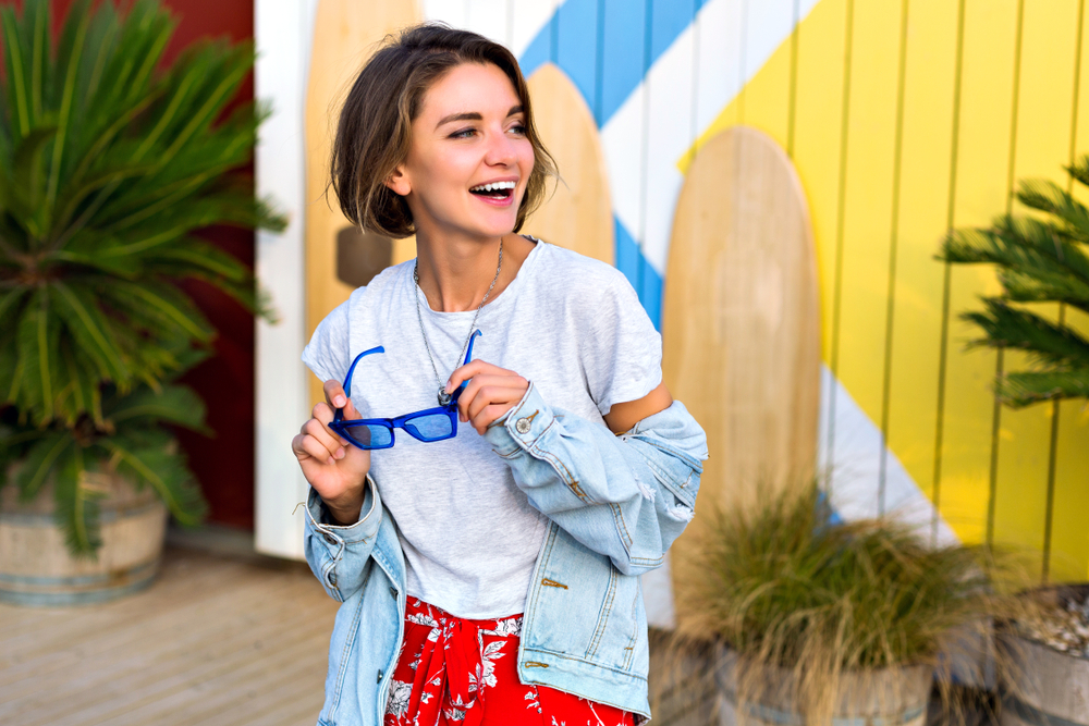 When wondering what to wear in Tampa, channel this model, who wears a cropped shirt, tropical shorts and a denim jacket for the spring in front of a beach shop. 