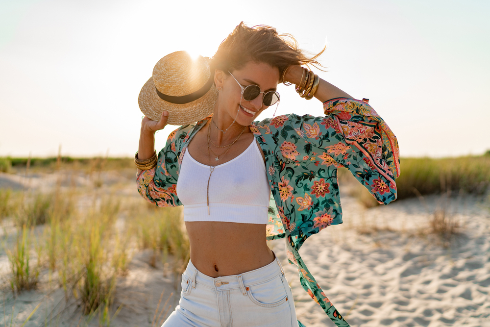 A woman knows what to wear in Tampa to the beach in her cropped white top, denim pants, sun hat, and a tie around cover. 