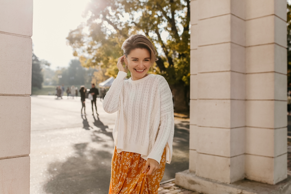 A woman poses as she wears a midi skirt that is orange with white florals and a white crew neck over it, enjoying the cooler weather and knowing what to wear in Tampa. 