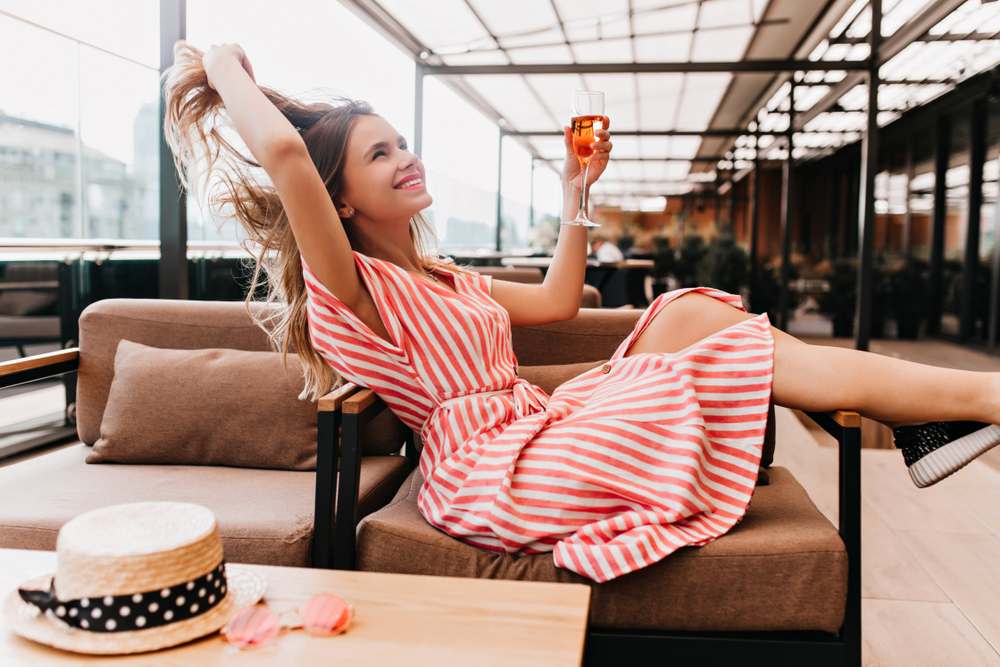 A woman enjoys a drink on a chair, wearing a striped midi dress, knowing exactly what to wear in Tampa. 