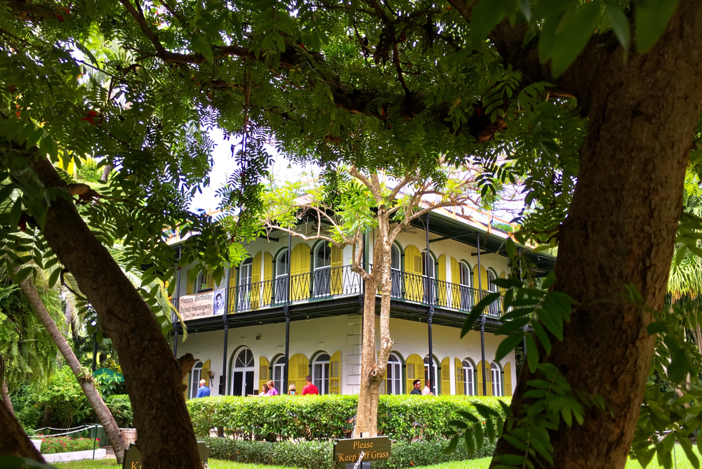 A photo of Ernest Hemingway's yellow home shows the house peaking through tree branches and a Happy Birthday sign hangs for the author on the balcony.