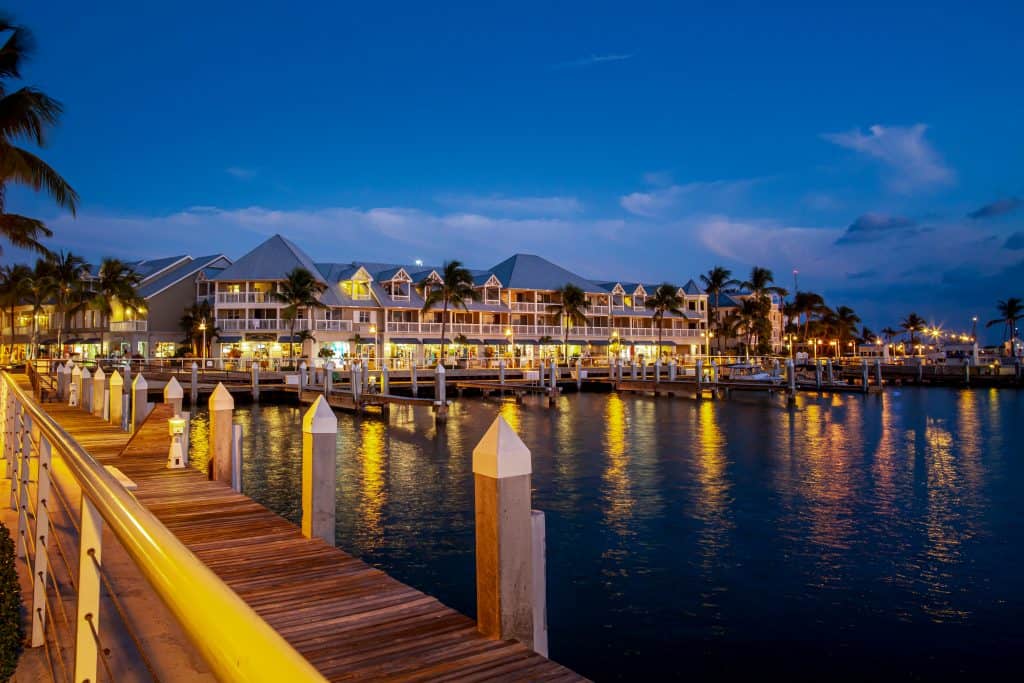 At night a hotel glistens in the dark, warm lights causing the street to glow by the docks and water.
