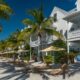 palm trees lining a street in key west florida with white buildings with balconies in the background and a blue sky