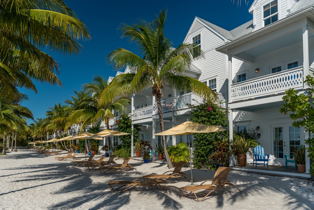 A photo of white villas on the beach lined with tanning chairs and palm trees and seaside views gives off the perfect Key West vibe.
