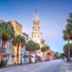 At dusk, the downtown area of Charleston is quaint and artsy, with fun colored buildings to explore. the street is lined with palm trees and there is a white church in the middle