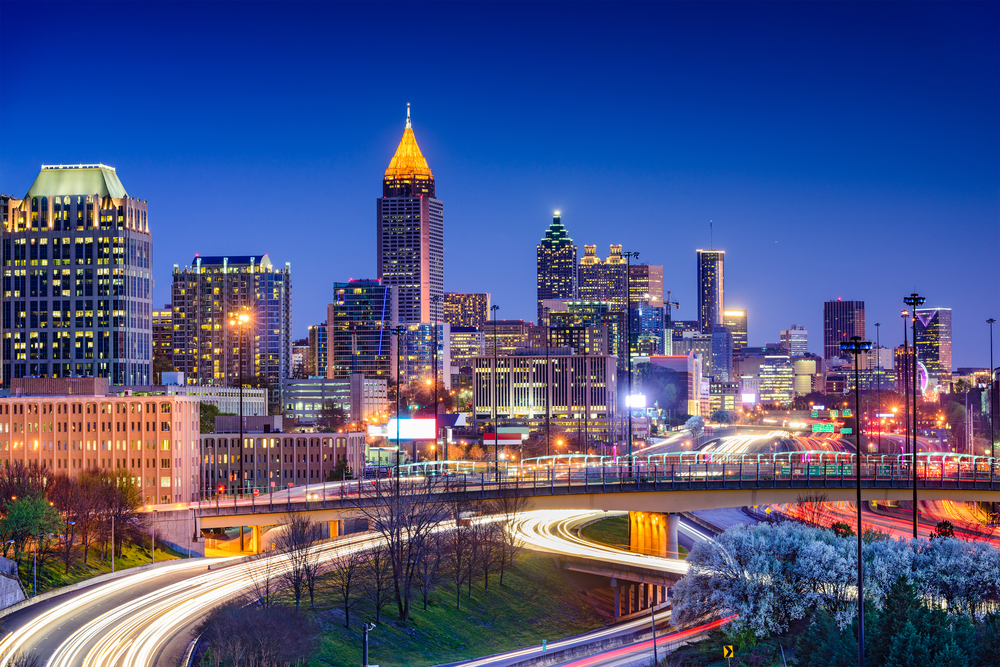 A night shot of Atlanta shows the city aglow with lights, cars zooming by on highways, and more.