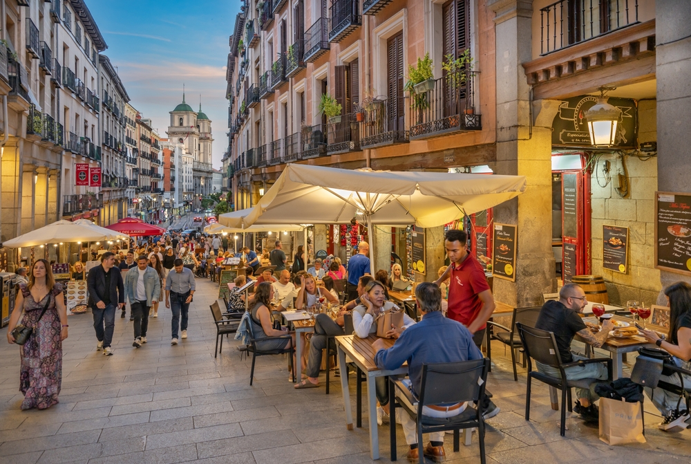 During dusk tourists and locals gather outside restaurants and cafes, enjoying time and meals together in Madrid.