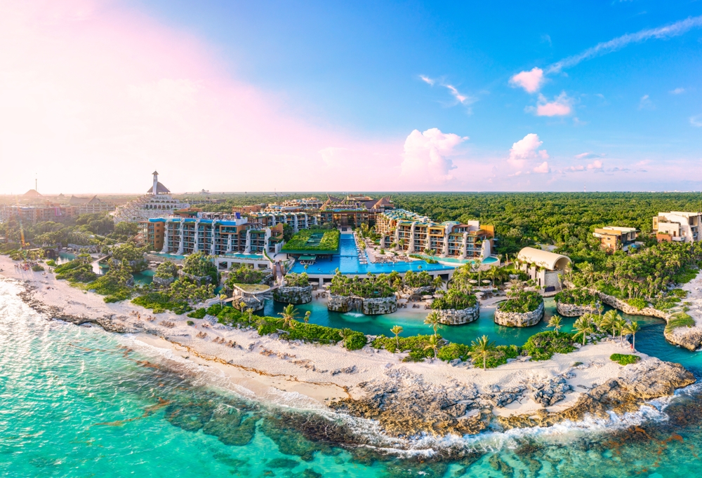 An overhead shot of Cancun shows the crystal clear water lapping against the shore as tall resorts tower beyond the coast, as a tropical oasis for tourists, since this is one of the cheapest places to fly from Orlando.