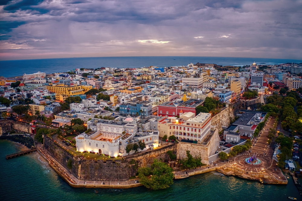 An ariel shot shows San Juan at dusk, lights turning on as the sun goes down, the vibrant buildings bright and fun and welcoming as one of the cheapest places to fly from Tampa. 